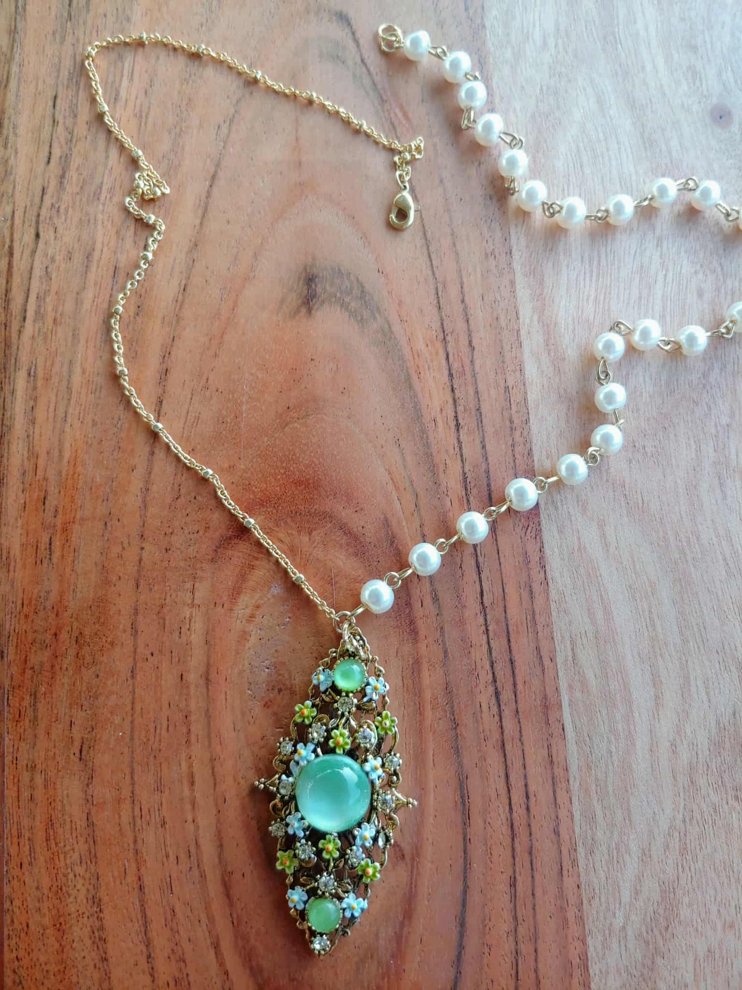 Necklace with a green pendant and pearl chain on a wooden surface
