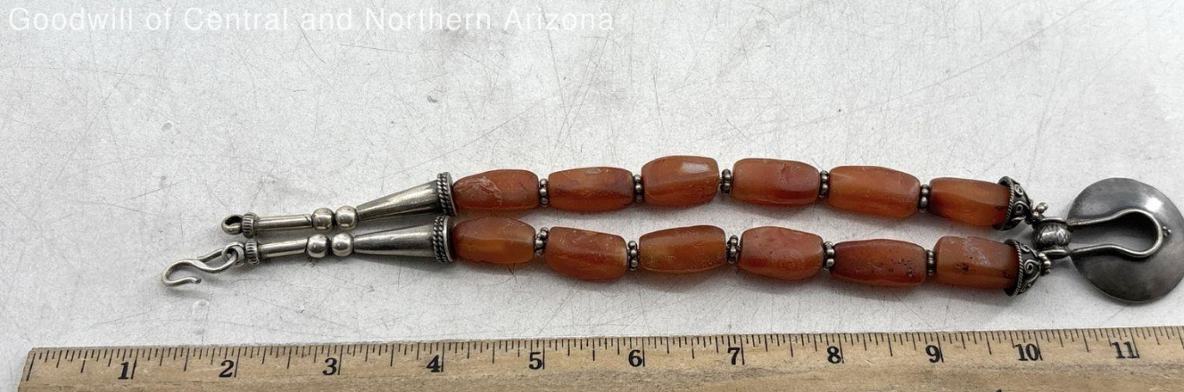 Red Stone and silver necklace next to ruler