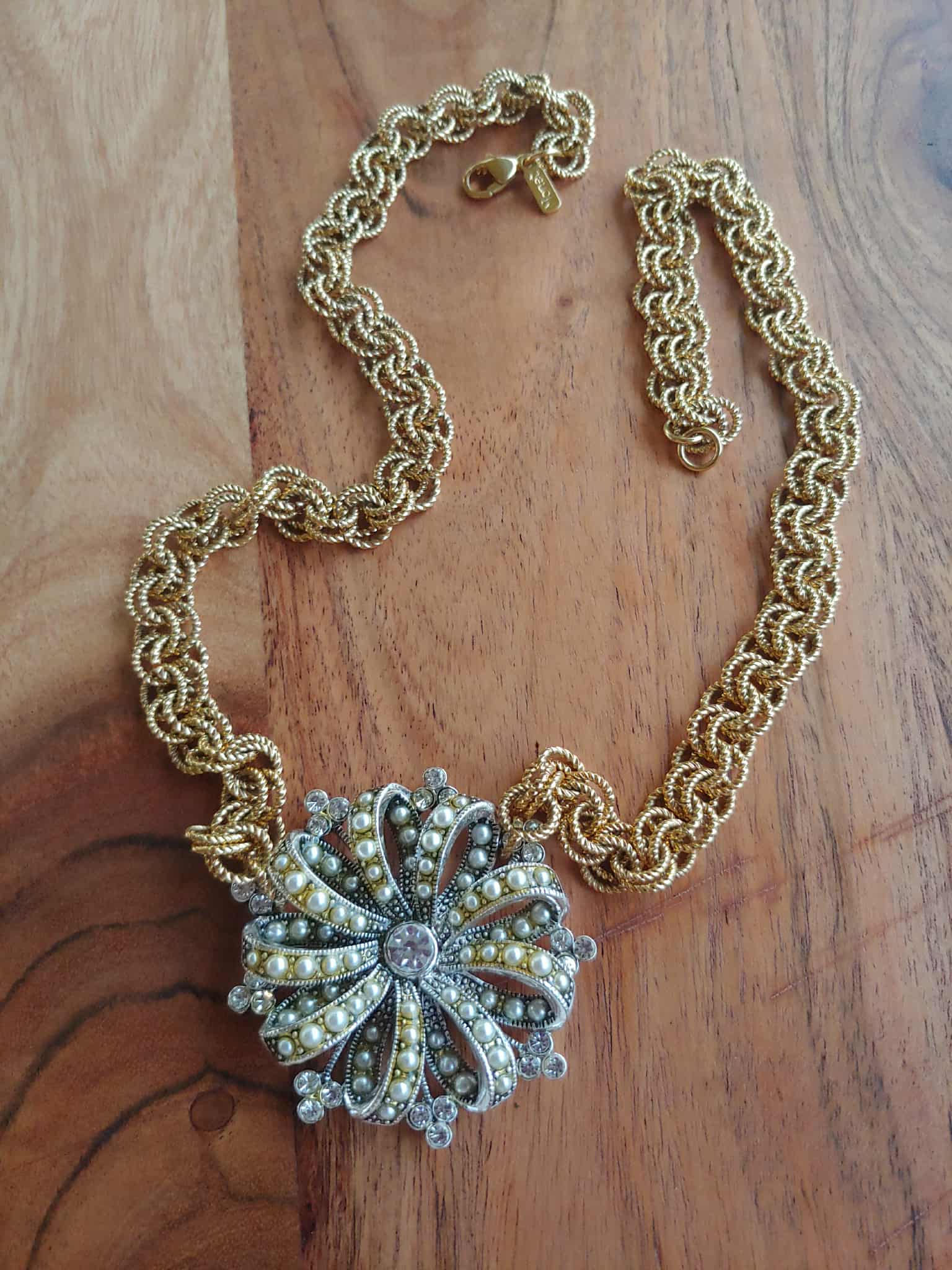 Gold chain necklace with a decorative silver pendant on a wooden surface