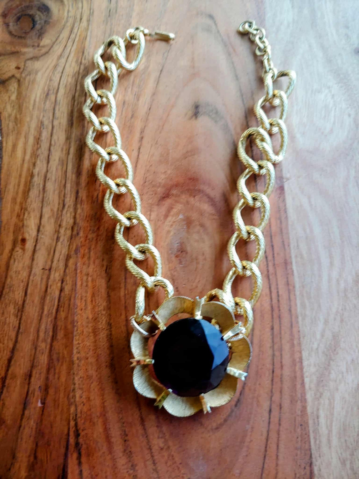 Gold chain necklace with a black pendant on a wooden surface