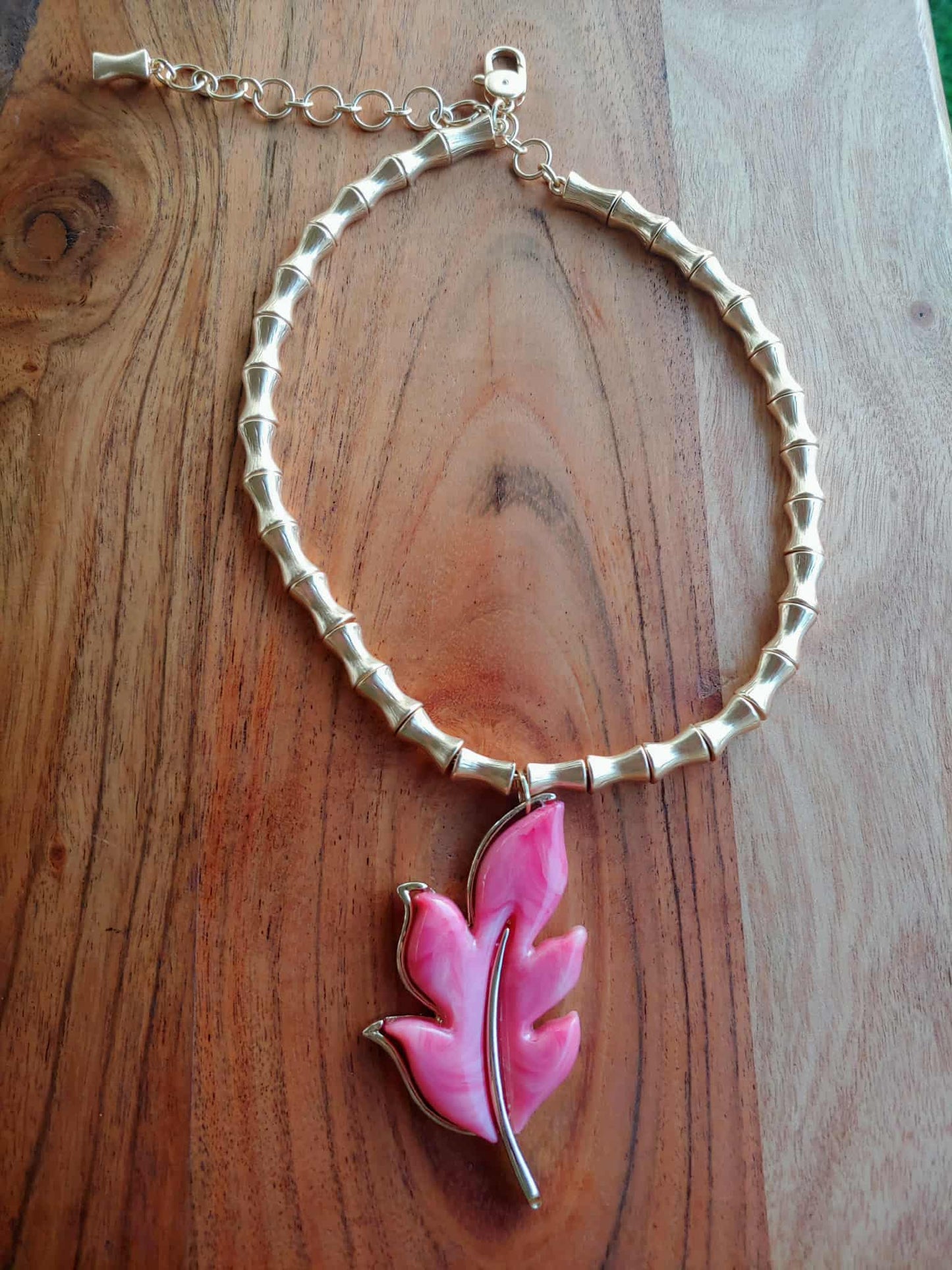 Necklace with a pink leaf-shaped charm on a wooden surface