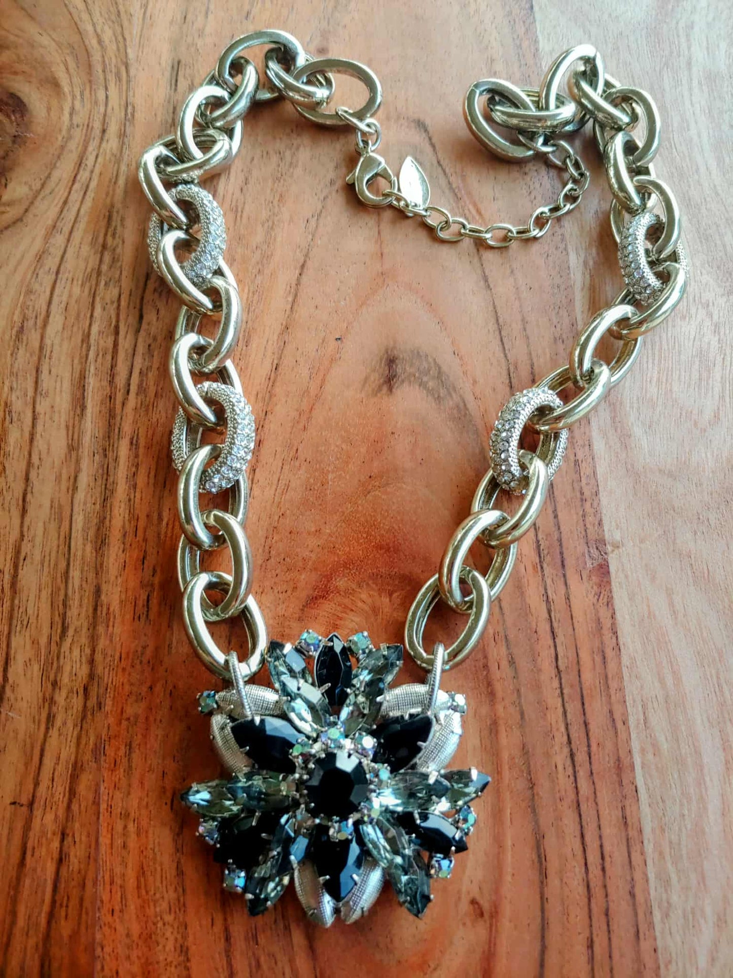 Gold chain necklace with a rhinestone pendant on a wooden surface