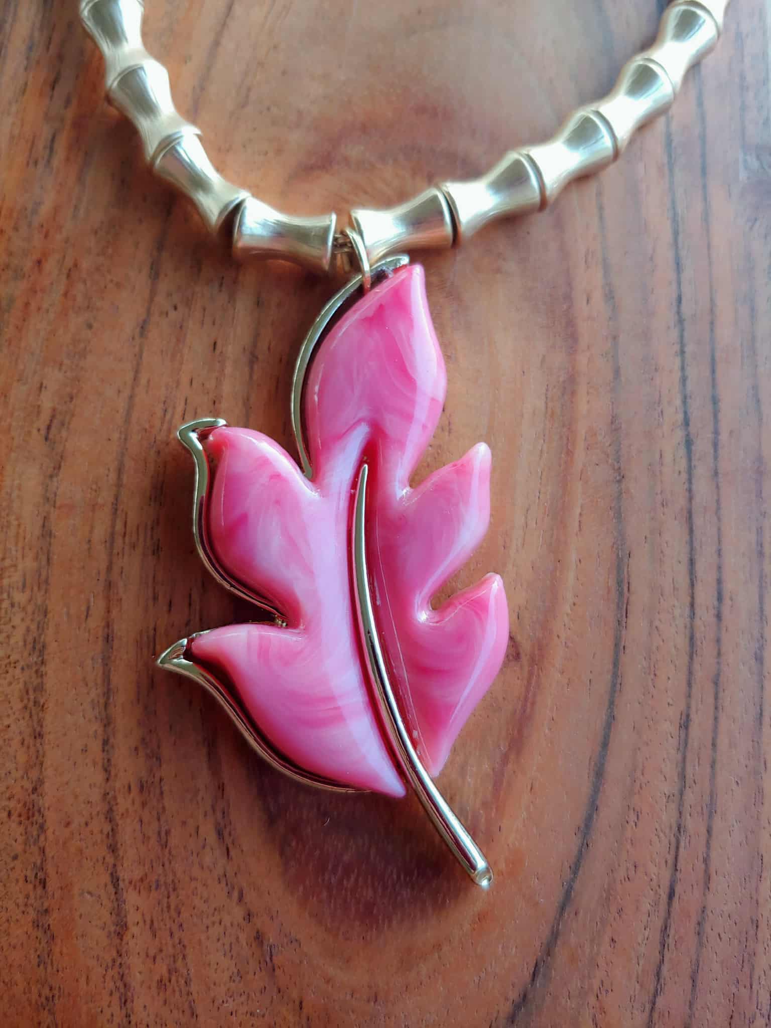 Pink leaf-shaped pendant on a gold chain against a wooden background