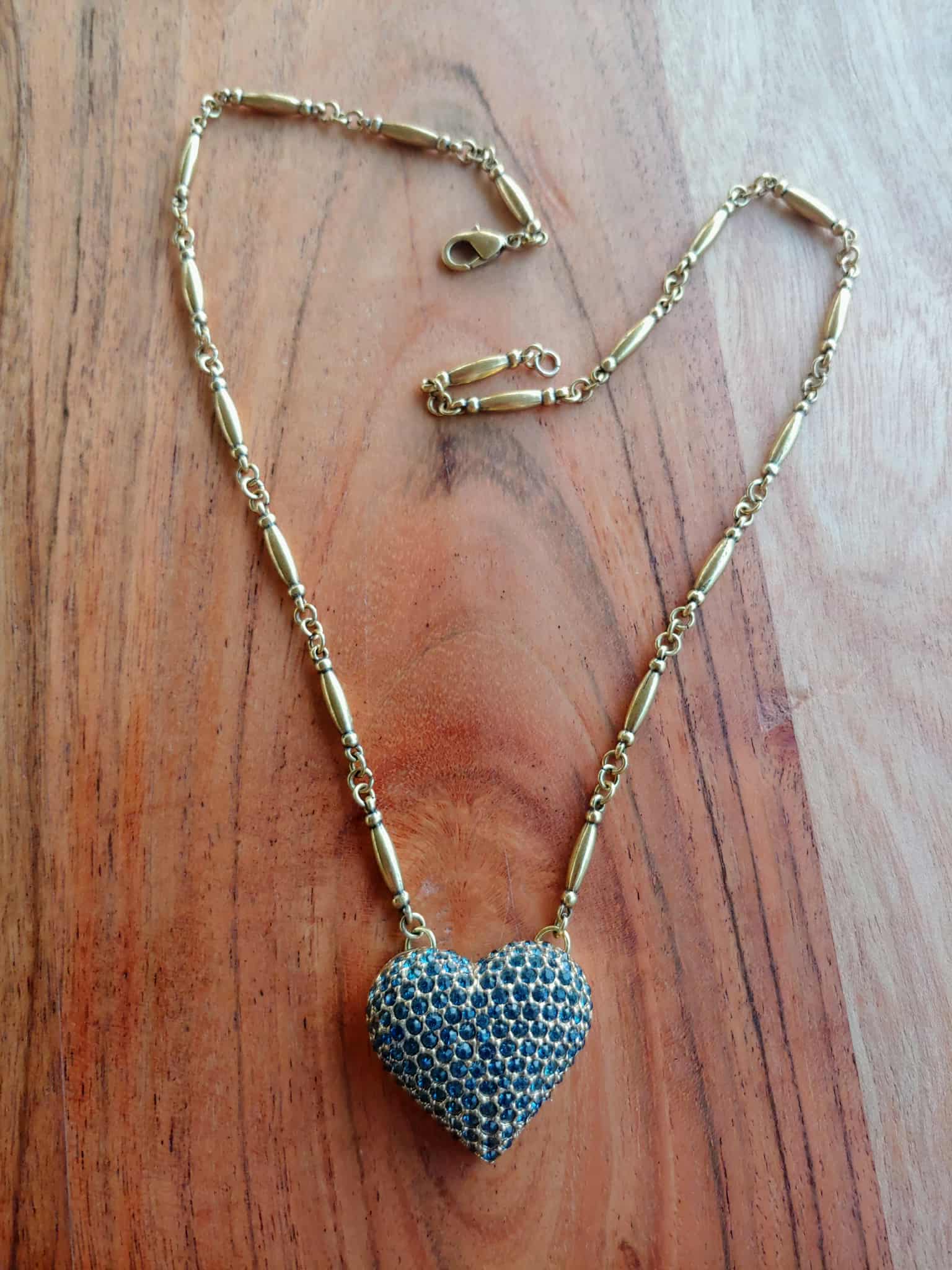 Gold necklace with a blue heart-shaped pendant on a wooden surface