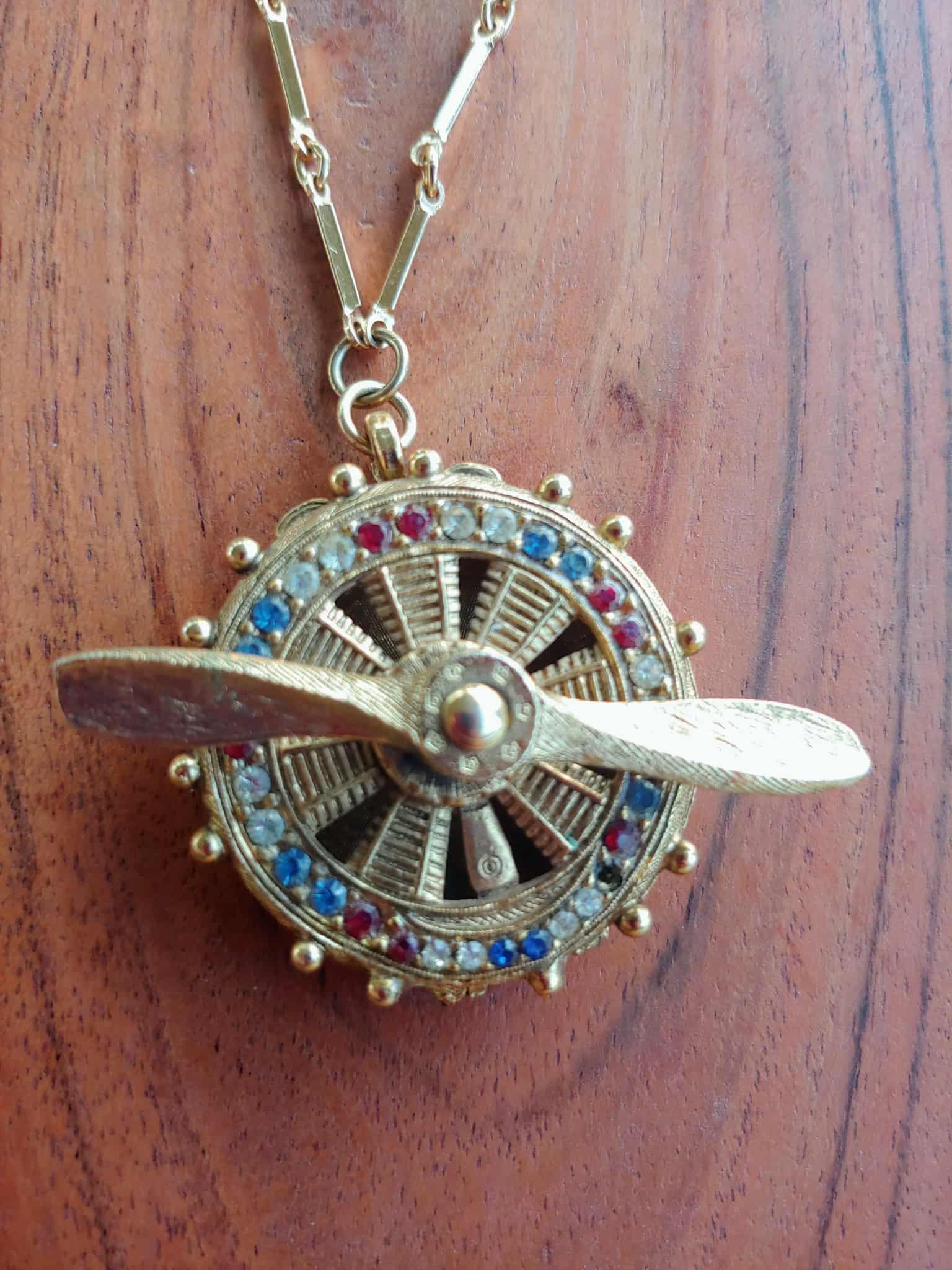 Gold necklace with a propeller pendant on a wooden surface