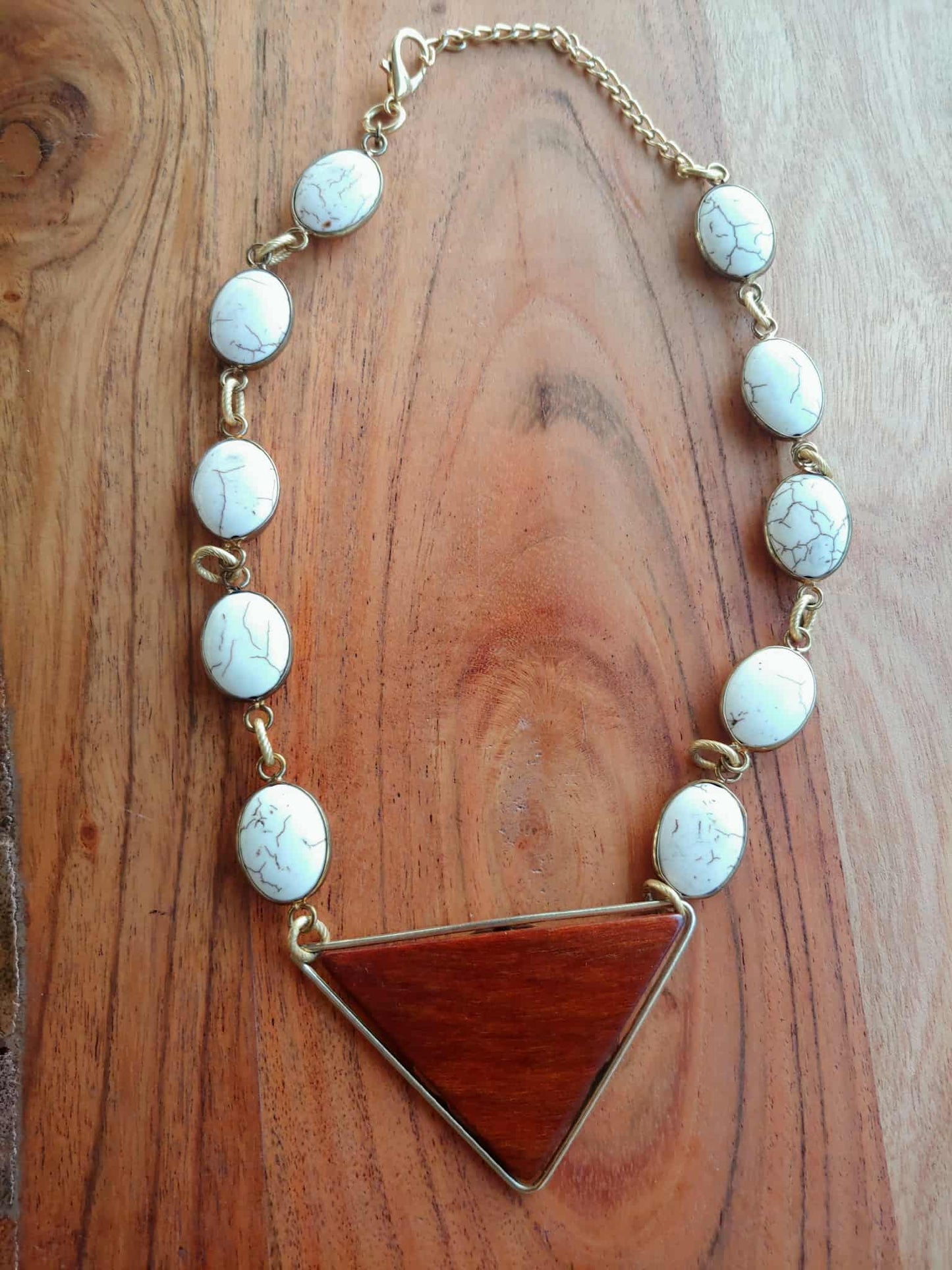 Necklace with white beads and a brown triangle pendant on a wooden surface