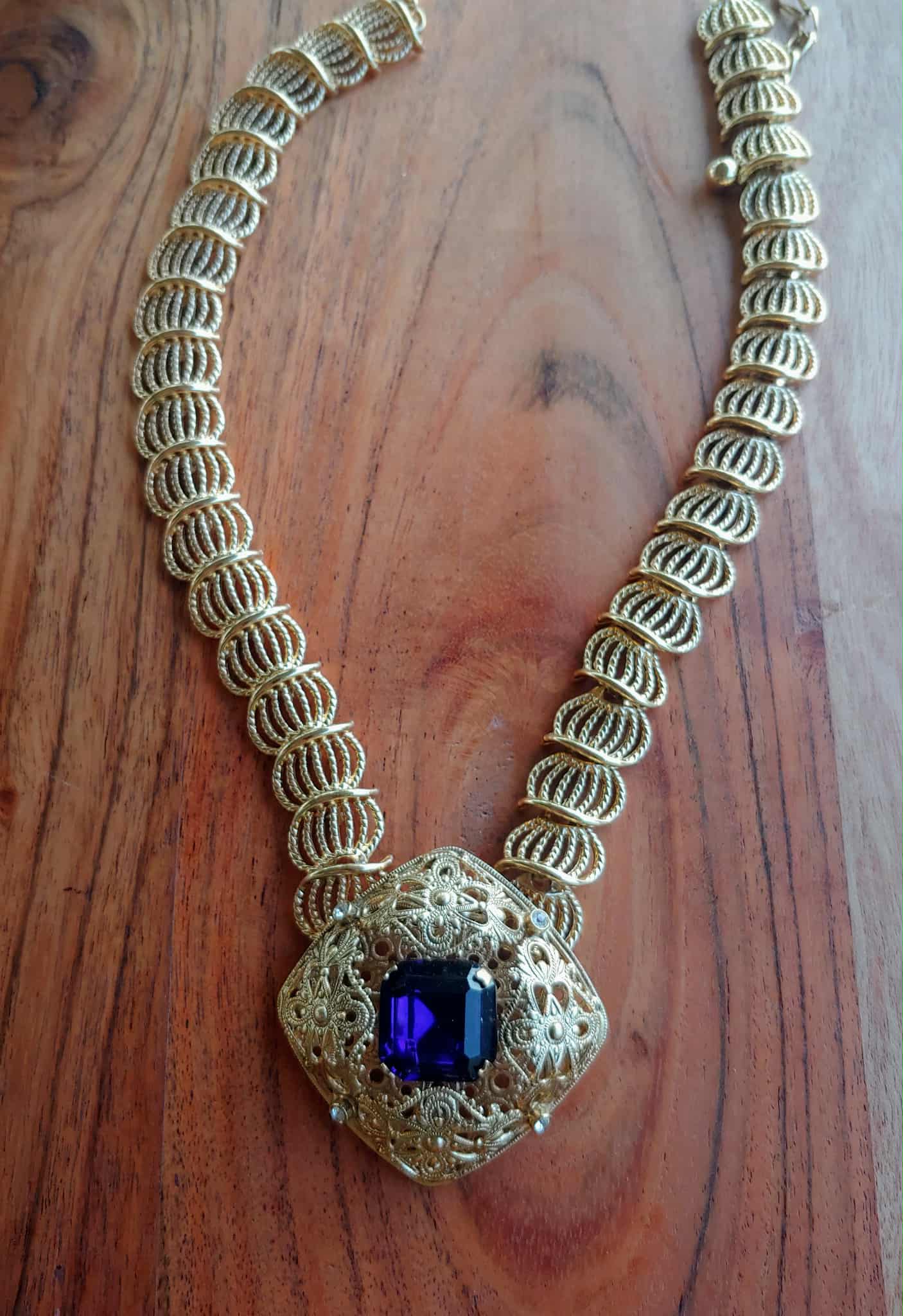 Gold necklace with a purple gemstone on a wooden surface