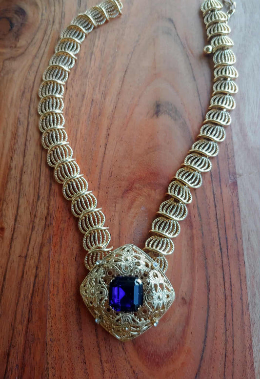 Gold necklace with a purple gemstone on a wooden surface