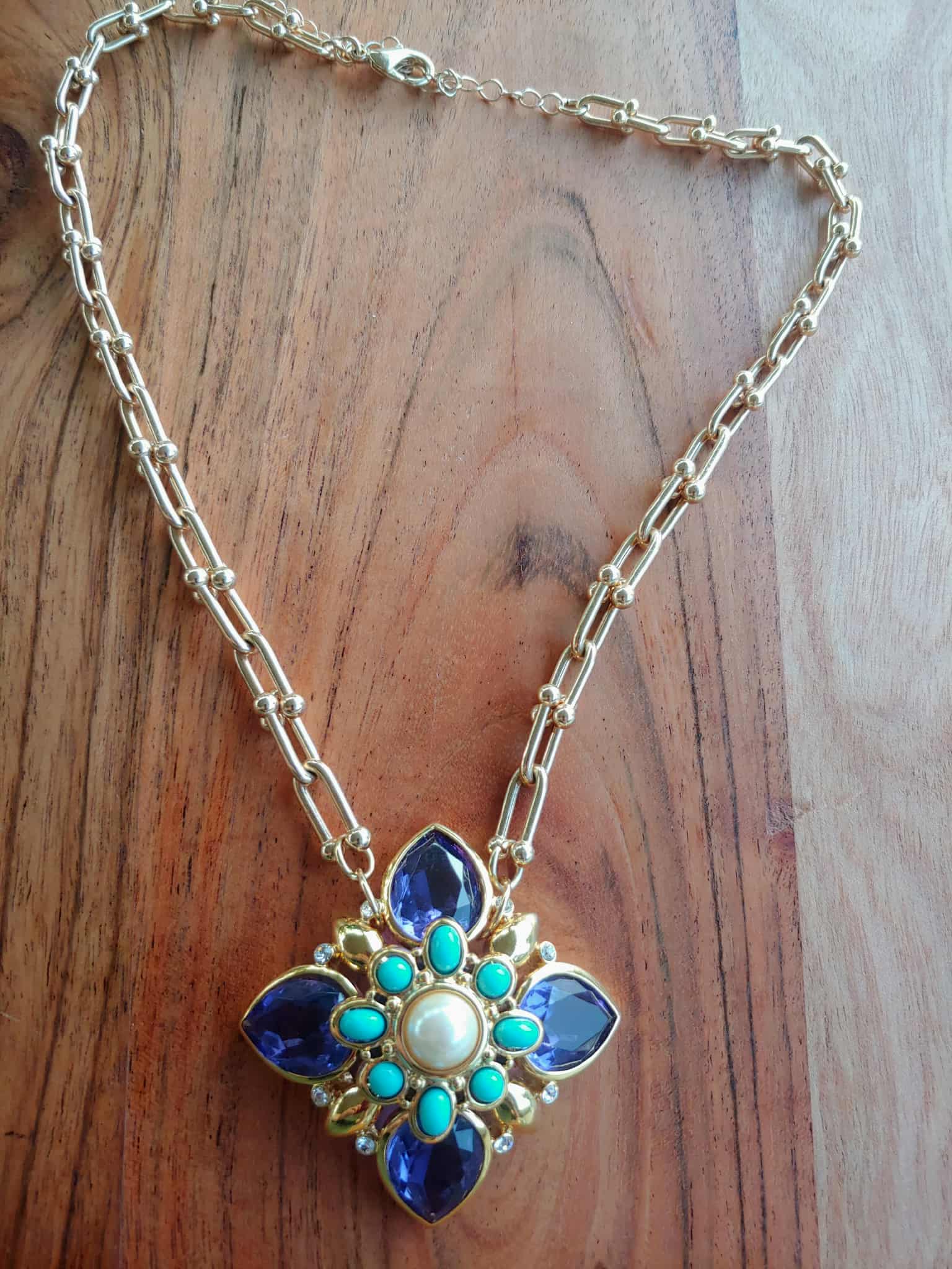 Necklace with a floral pendant featuring blue and turquoise stones on a wooden surface