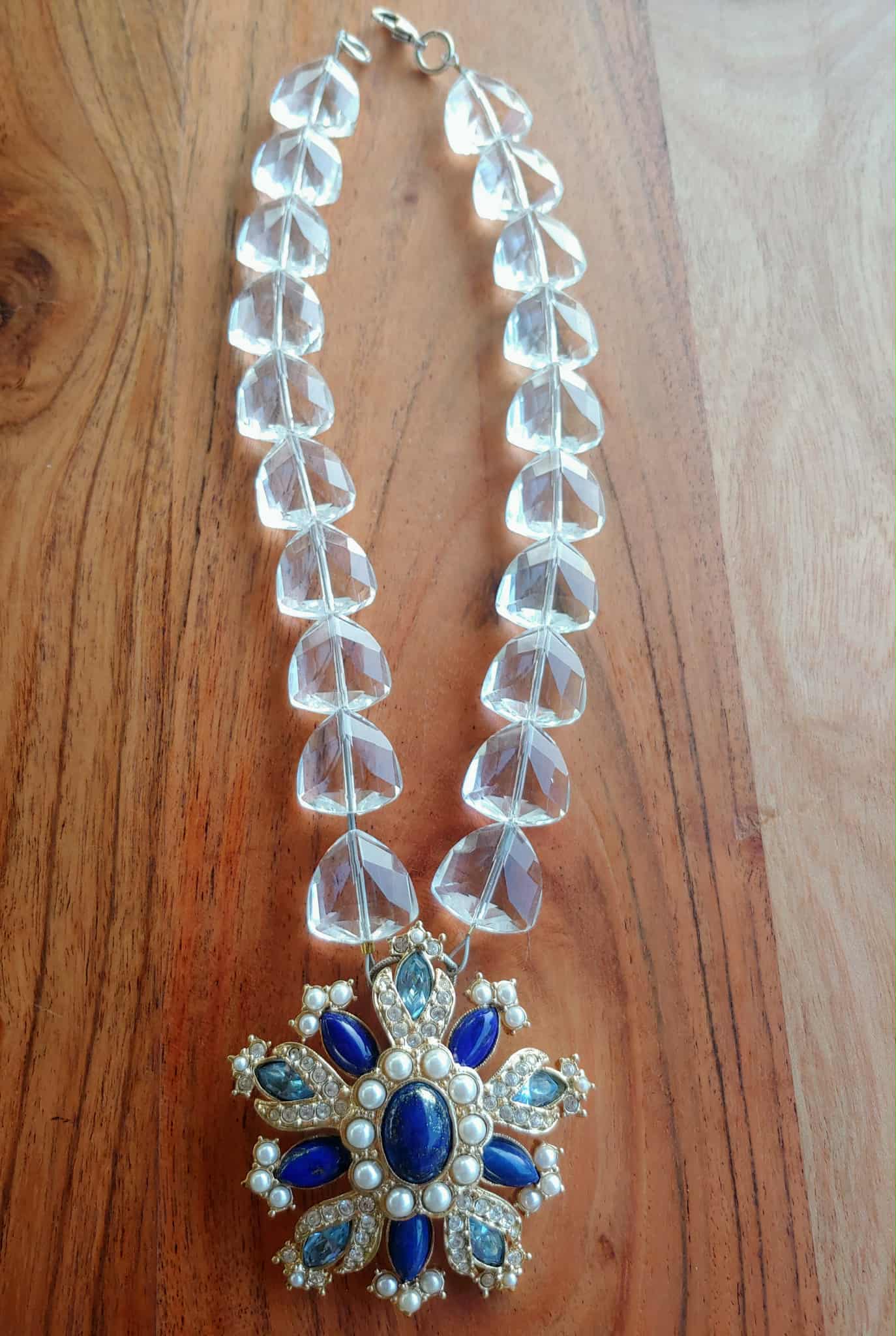Necklace with clear beads and a blue and silver pendant on a wooden surface