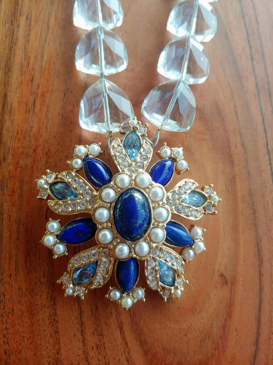 Decorative pendant with blue stones and pearls on a wooden surface