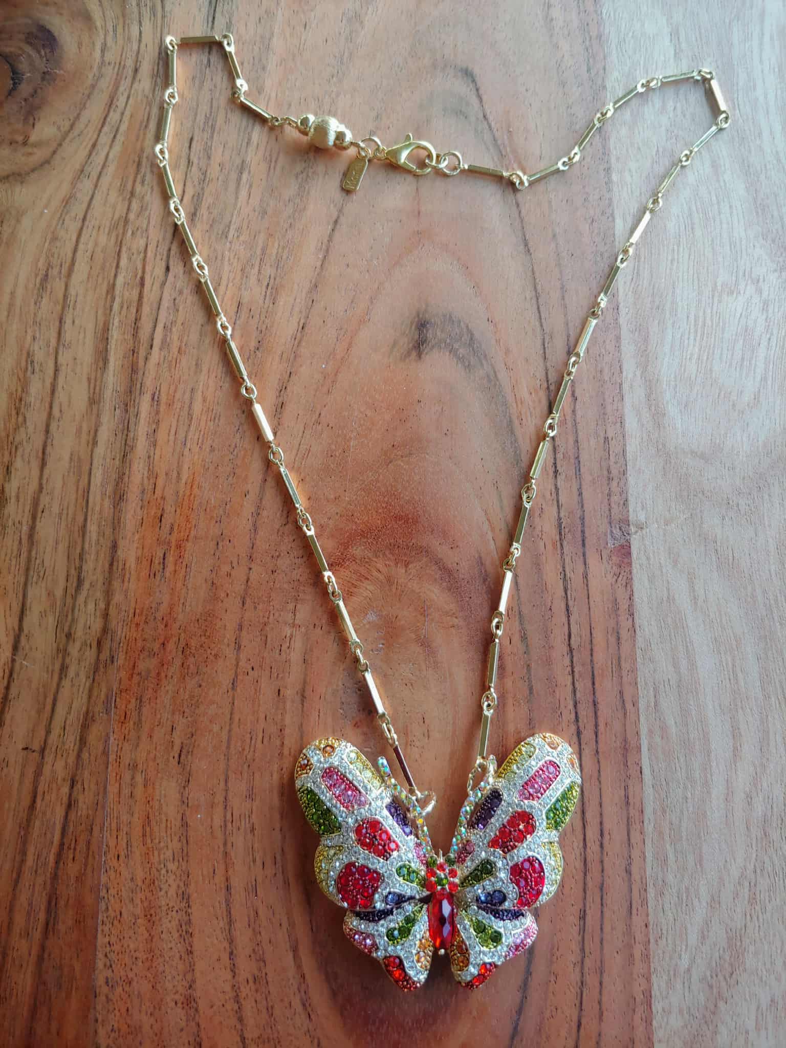 Butterfly-shaped pendant on a gold chain against a wooden background