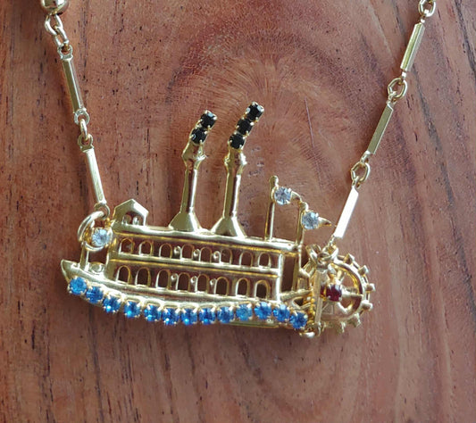 Gold necklace with a ship-shaped pendant on a wooden surface