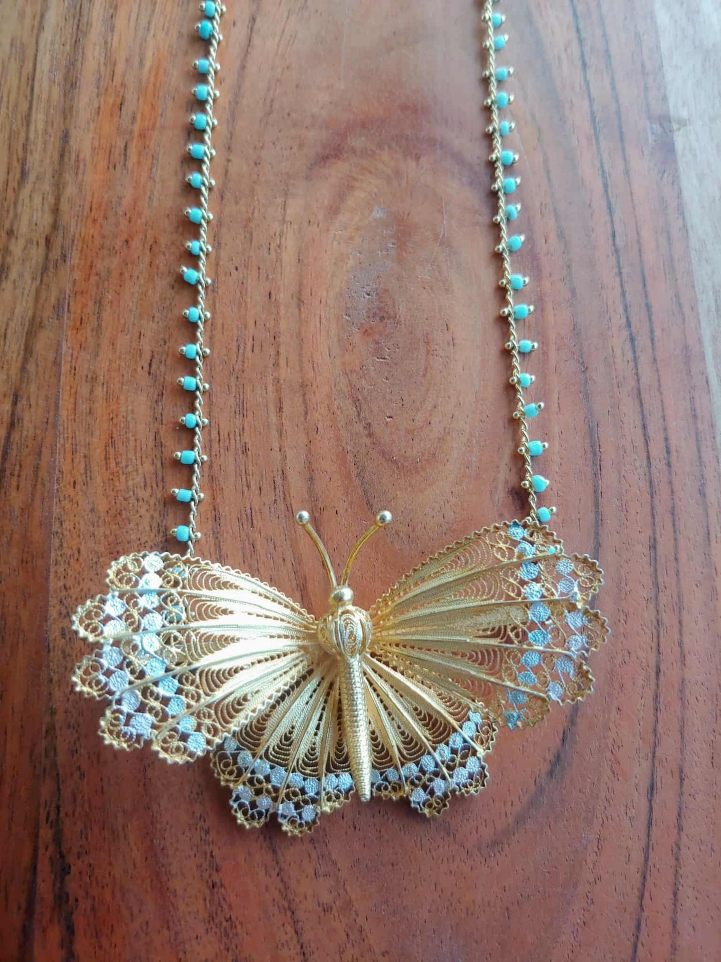 Gold butterfly necklace with turquoise beads on a wooden surface
