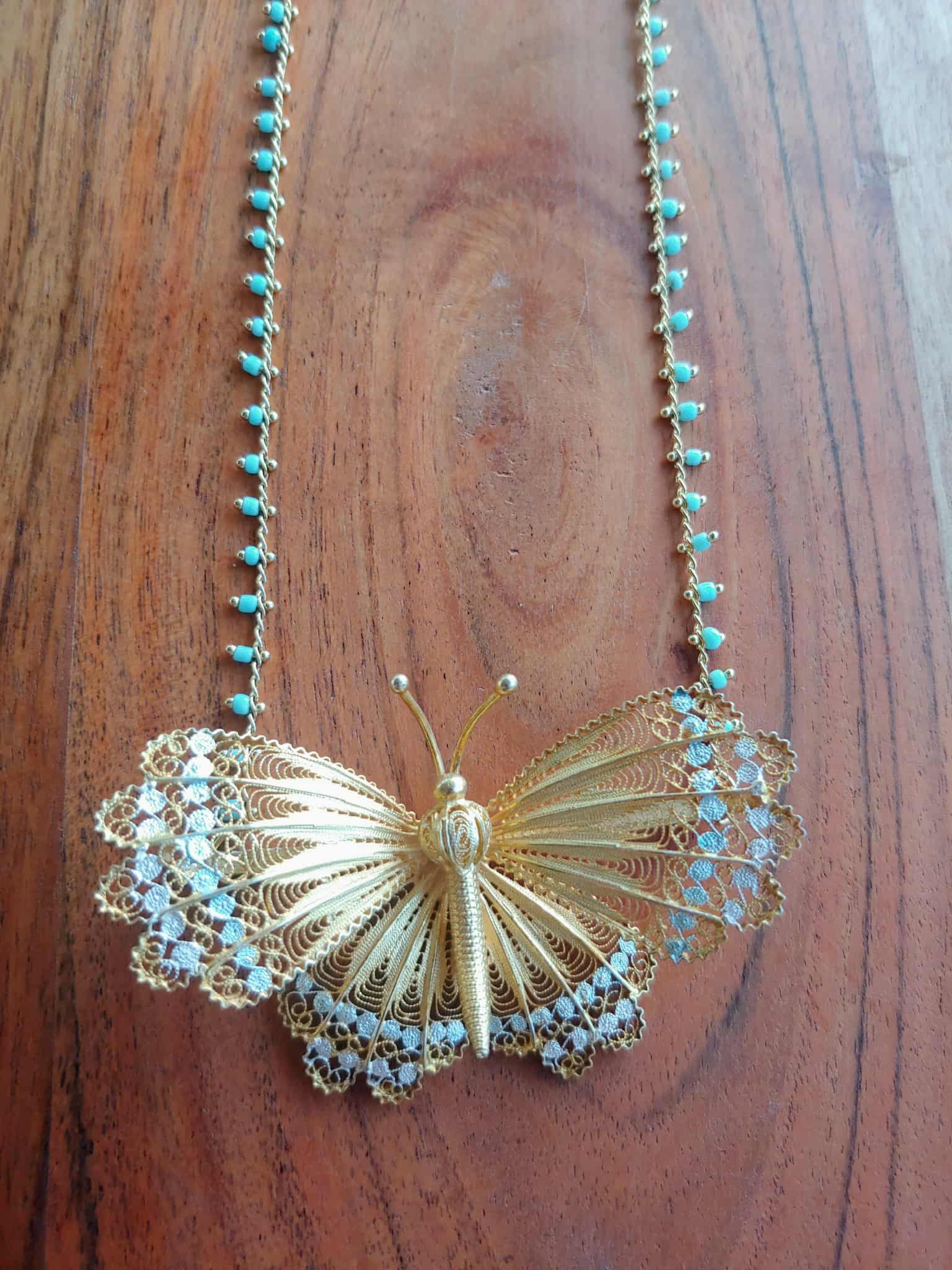 Gold butterfly necklace with turquoise beads on a wooden surface