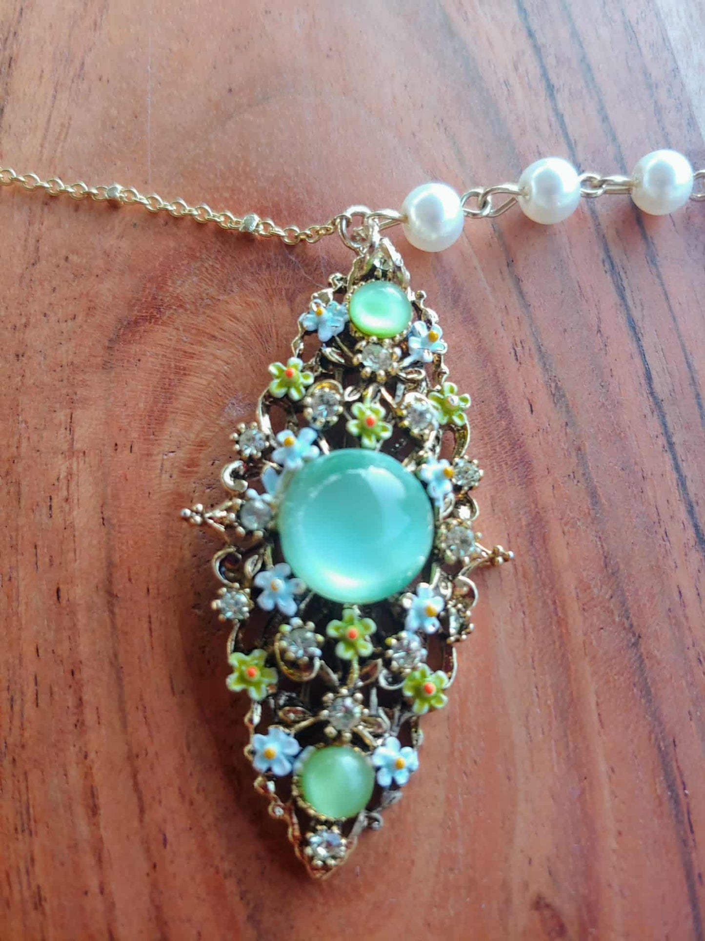Necklace with a decorative pendant featuring green stones and pearls on a wooden surface