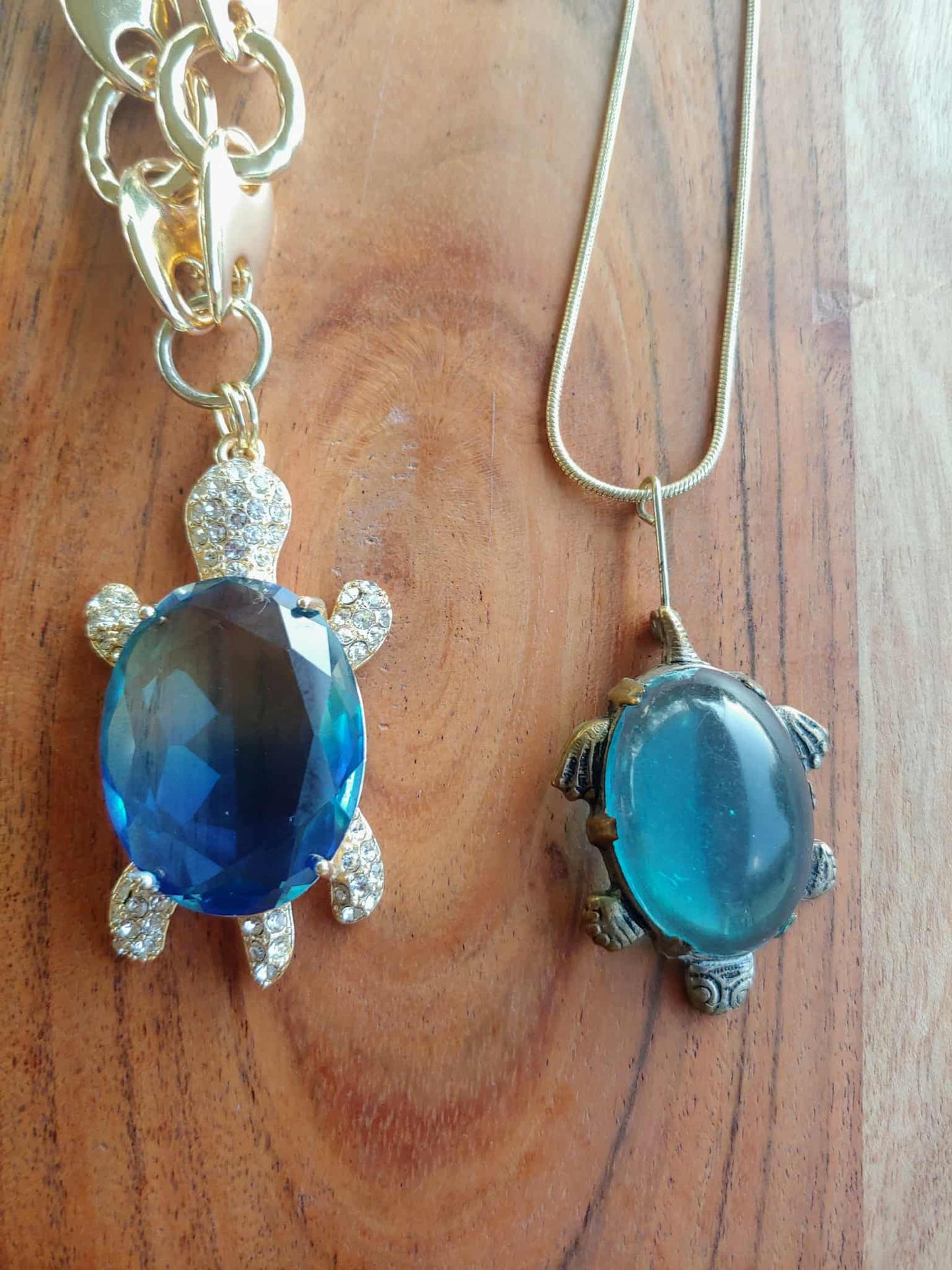 Two turtle-shaped pendants with blue gemstones on a wooden surface