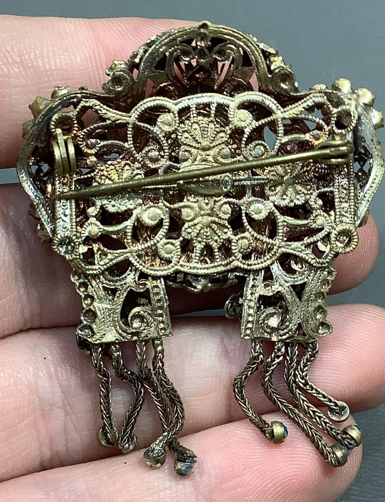 Gold filigree brooch held in a hand against a neutral background