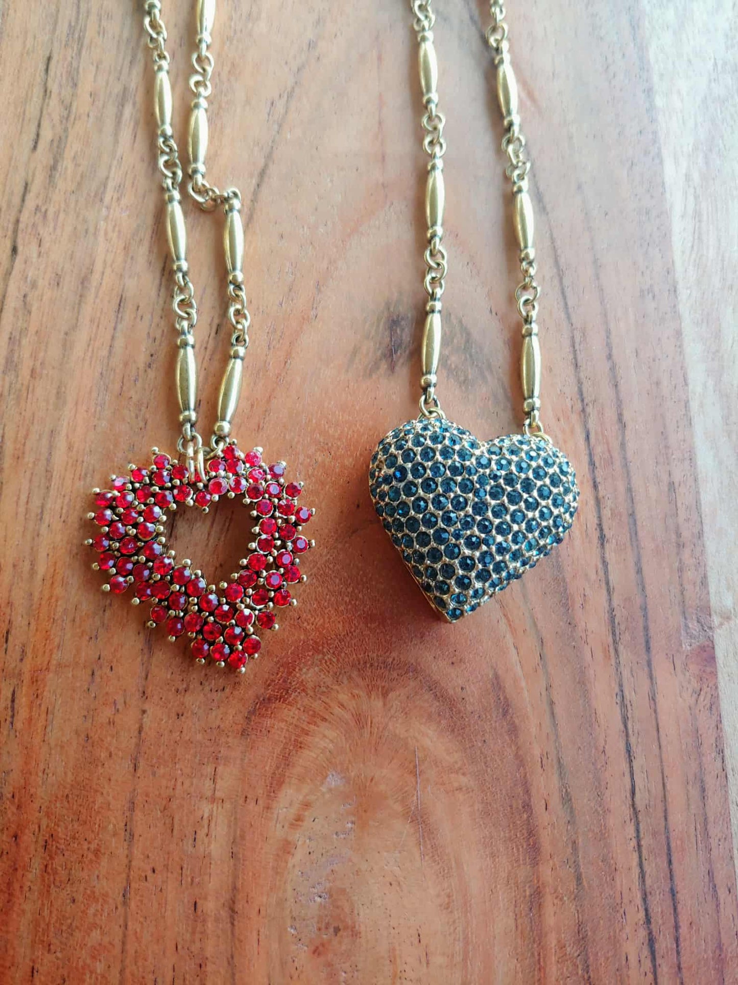 Two heart-shaped pendants on chains against a wooden background