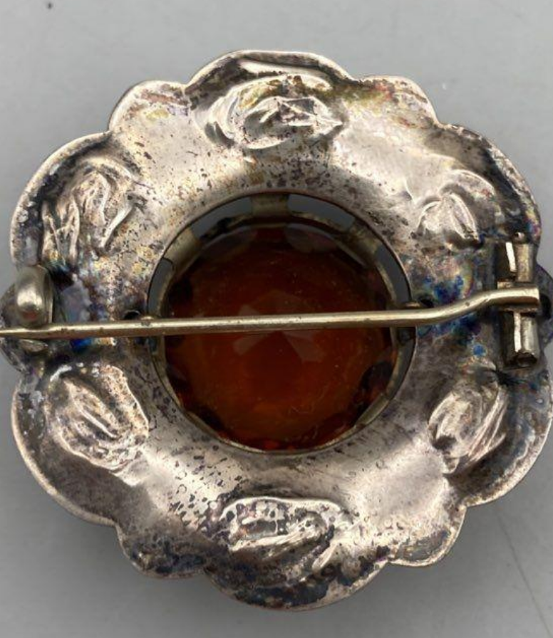 Silver brooch with a central amber stone on a gray background