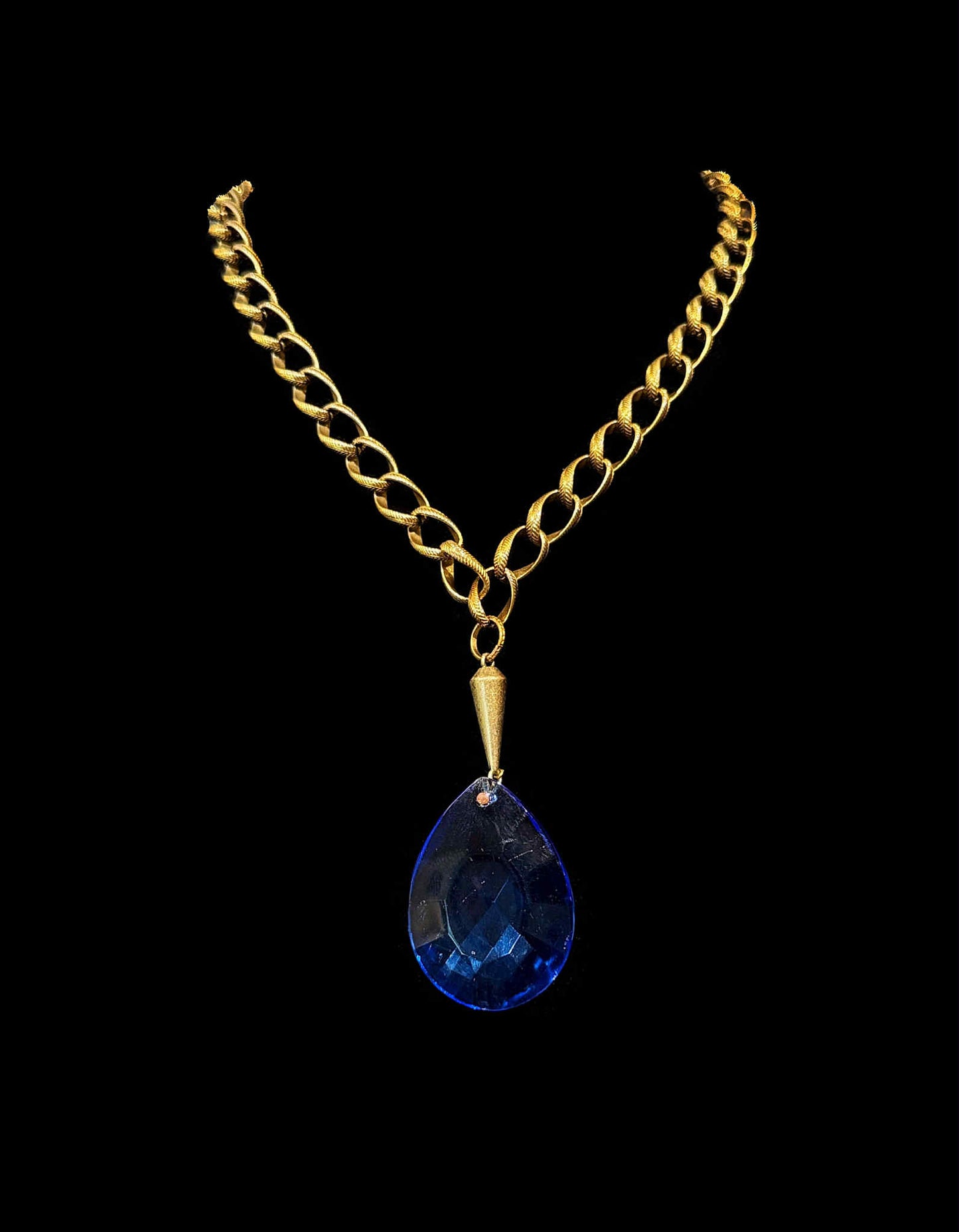 Gold chain necklace with a blue teardrop pendant on a black background
