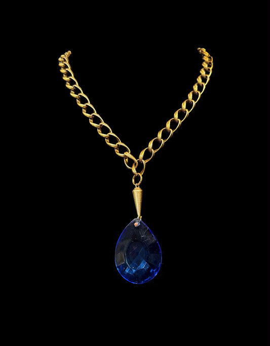 Gold chain necklace with a blue teardrop pendant on a black background