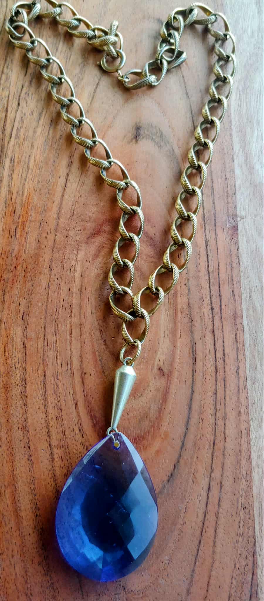 Gold chain necklace with a blue teardrop pendant on a wooden surface