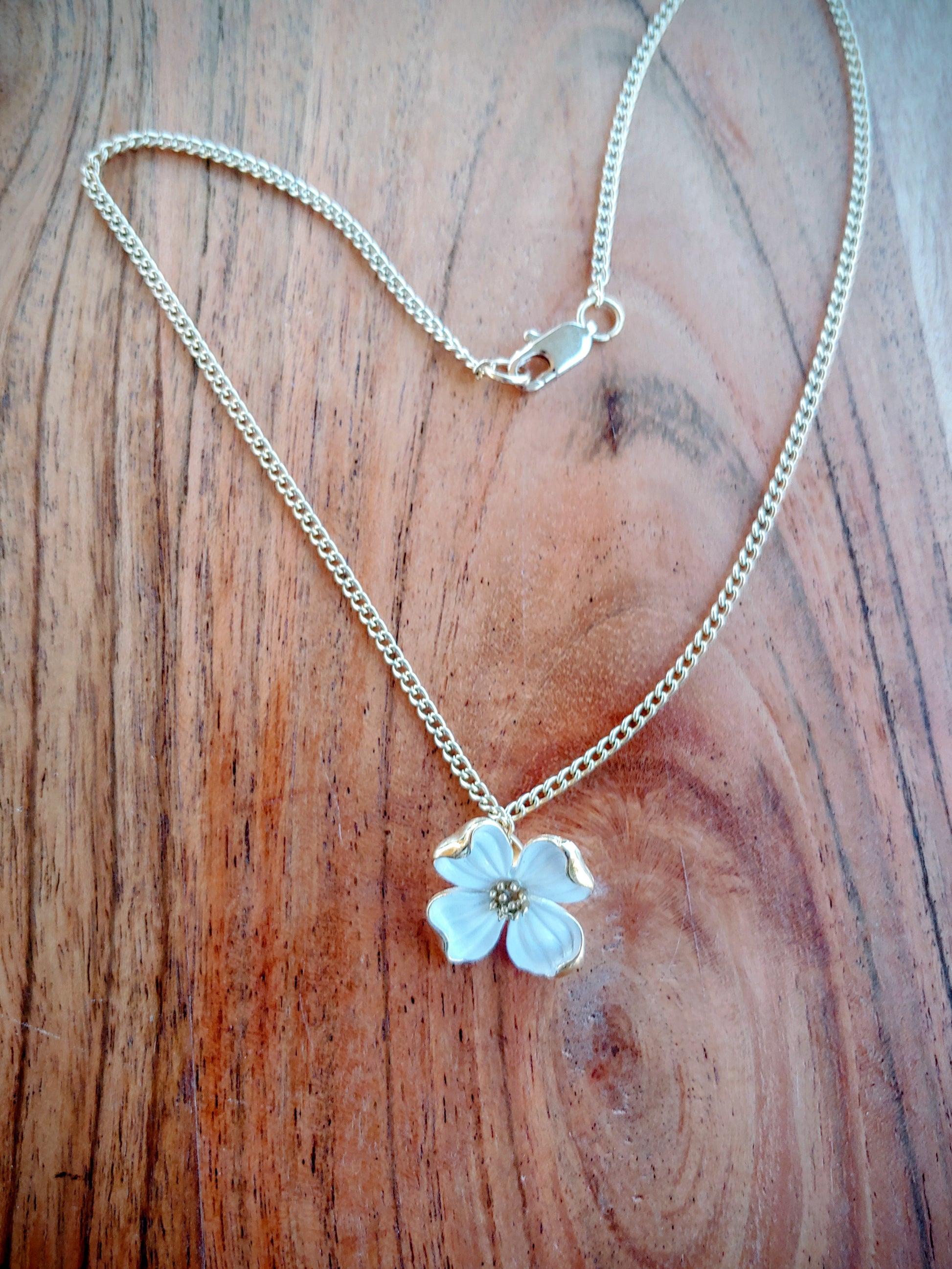 Gold necklace with a white flower pendant on a wooden surface