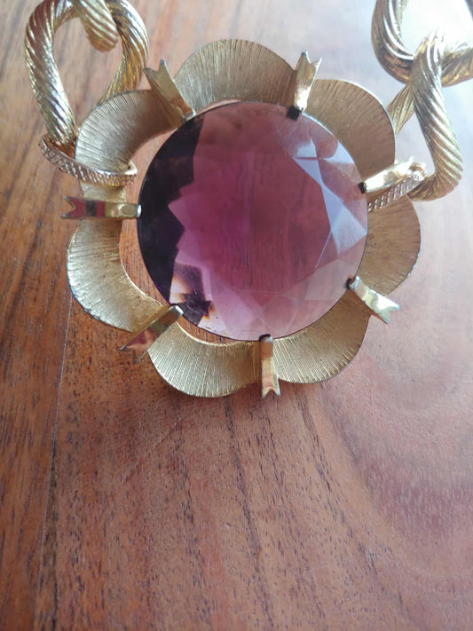 Gold brooch with a pink gemstone on a wooden surface
