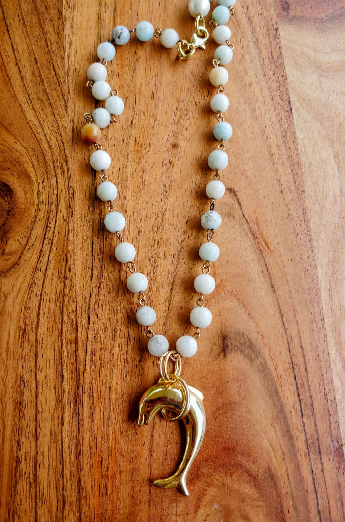 Necklace with white beads and a gold dolphin pendant on a wooden surface