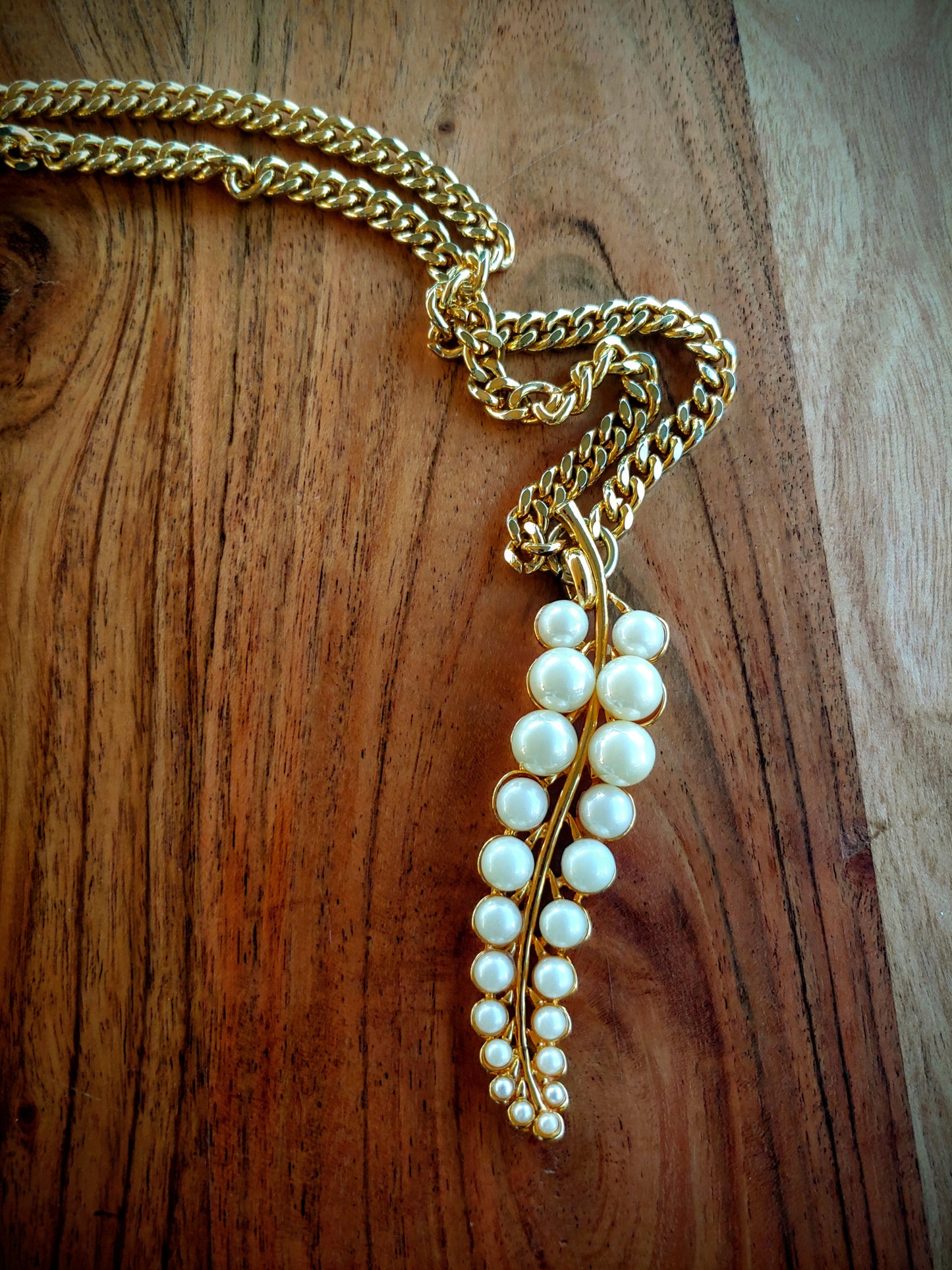 Gold chain necklace with a pearl pendant on a wooden surface