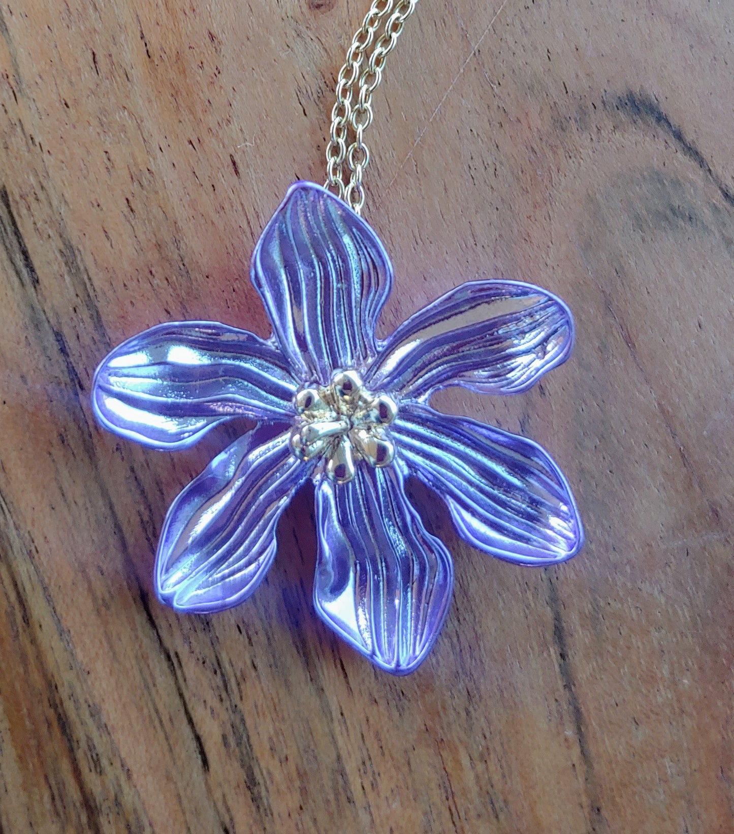 Purple flower-shaped pendant on a chain against a wooden background