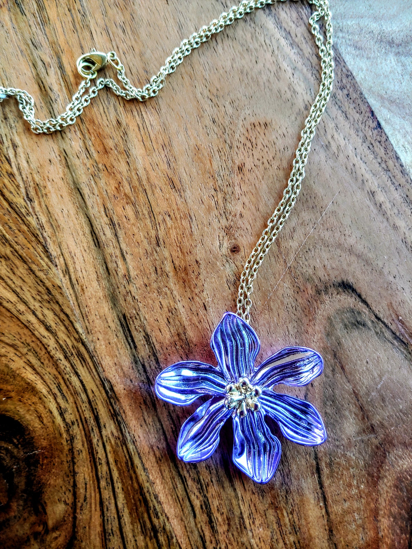 purple flower-shaped pendant on a chain against a wooden background