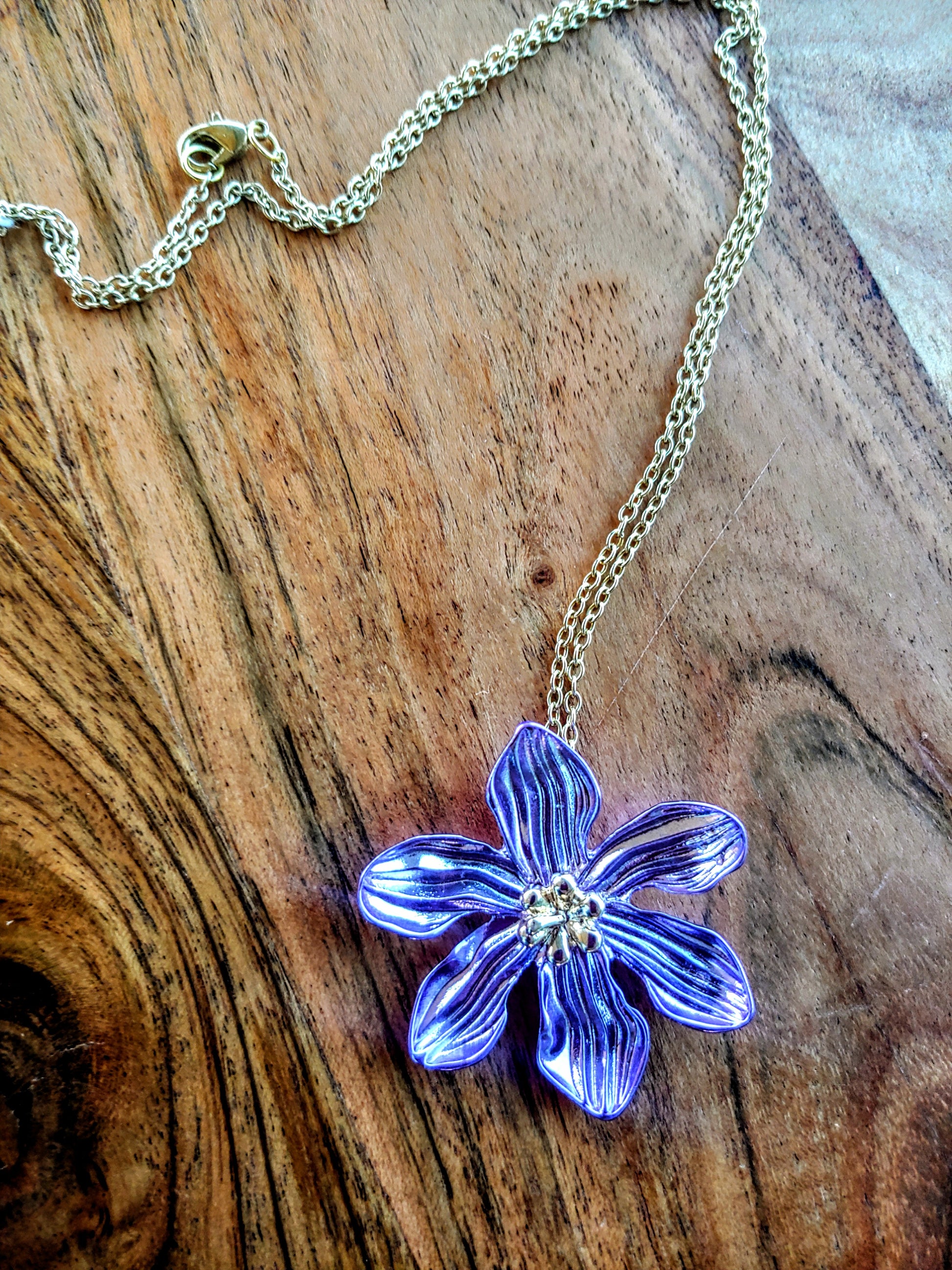 purple flower-shaped pendant on a chain against a wooden background