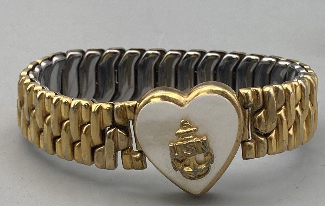 Gold bracelet with a heart-shaped charm featuring a logo on a gray background