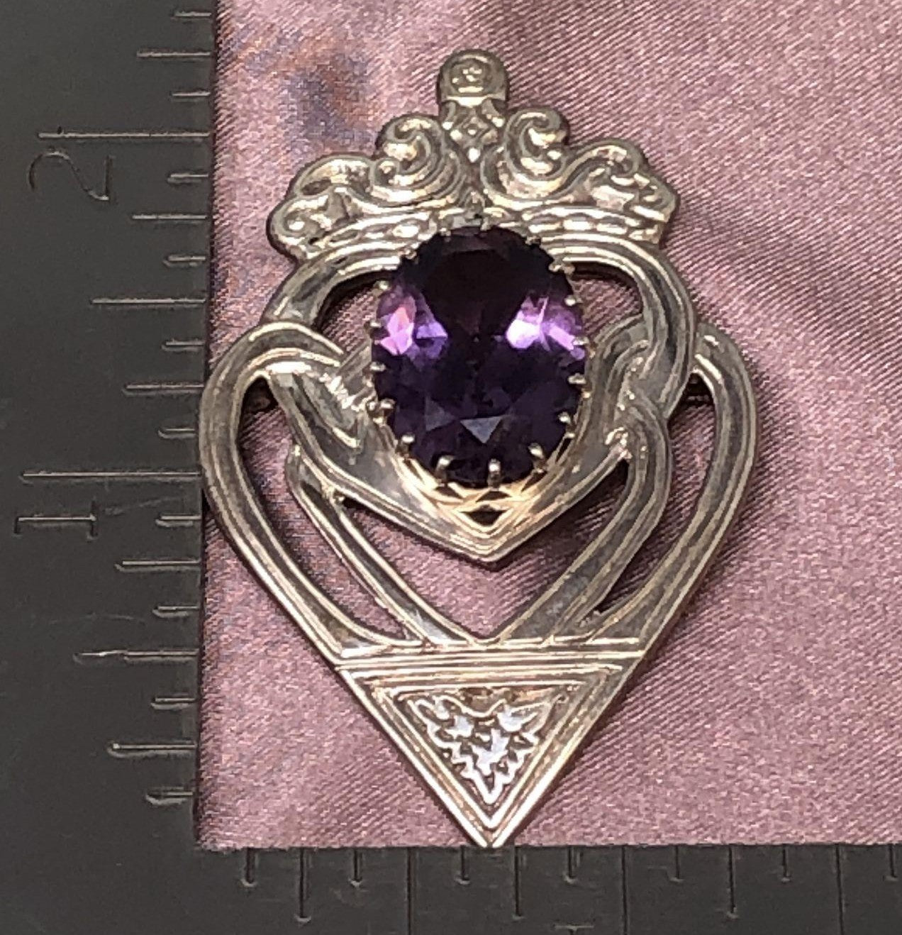 Ruler next to purple and silver brooch on pink cloth