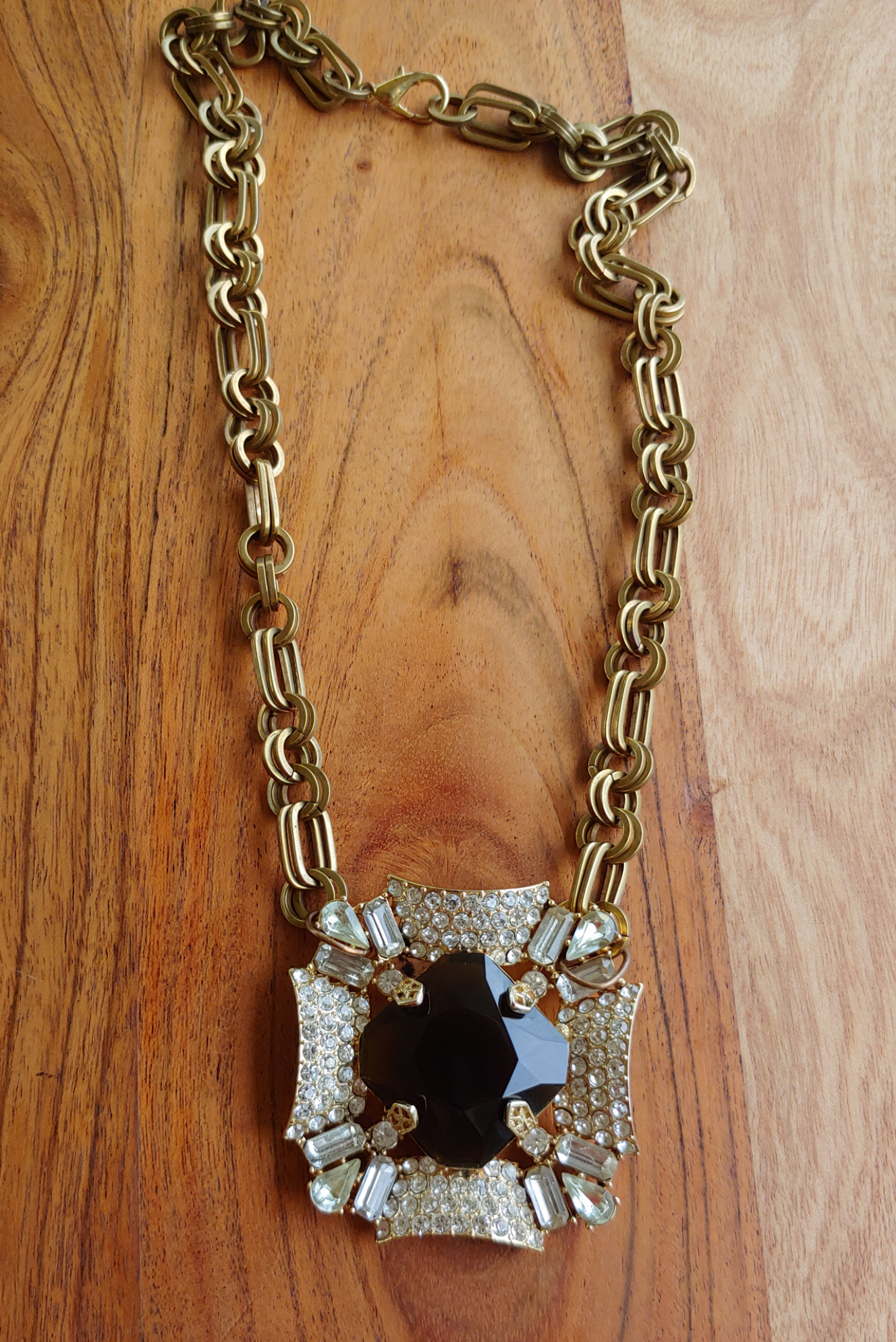 Gold necklace with a pendant featuring a central black stone and smaller clear stones on a wooden surface