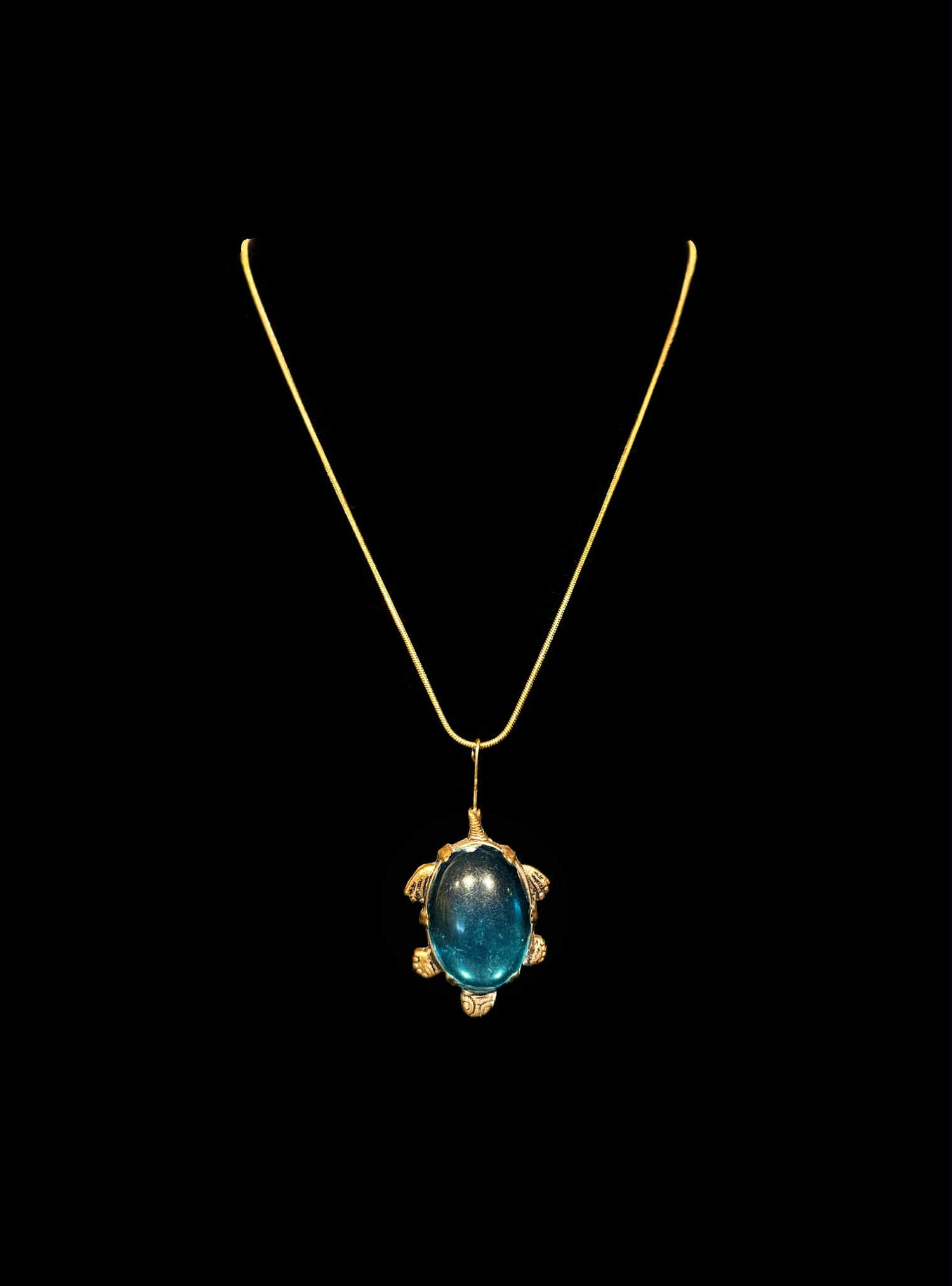 Gold pendant with a blue gemstone on a black background