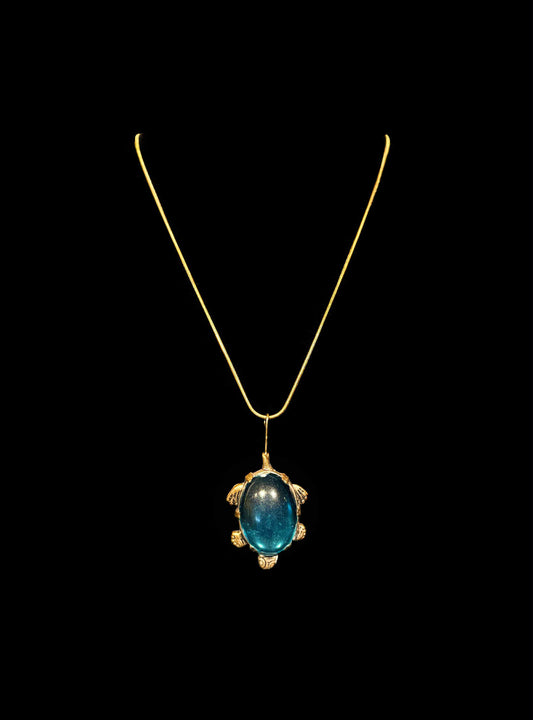 Gold pendant with a blue gemstone on a black background
